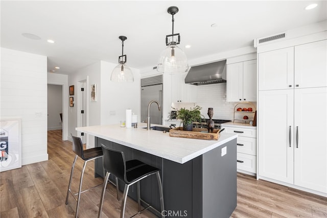 kitchen with backsplash, wall chimney range hood, visible vents, a sink, and built in refrigerator