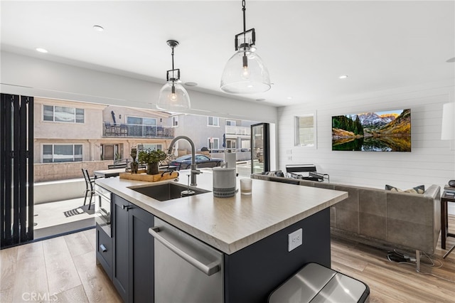 kitchen featuring a sink, open floor plan, dishwasher, a center island with sink, and light wood finished floors