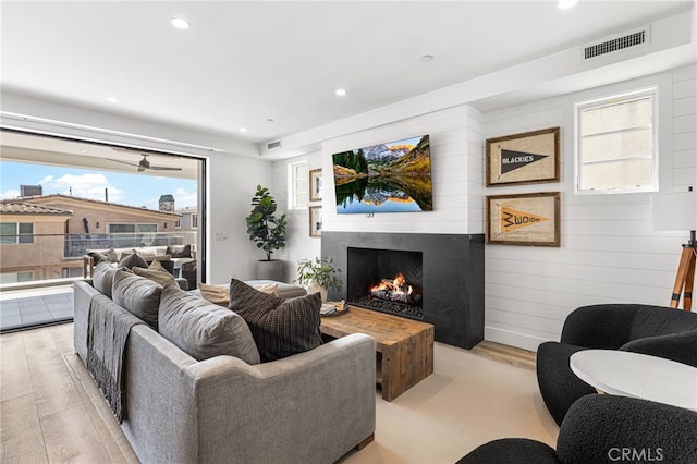 living area featuring light wood-style flooring, visible vents, a wealth of natural light, and a lit fireplace