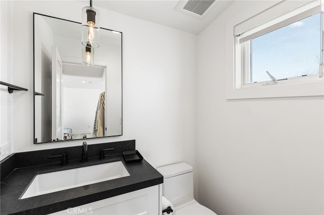 bathroom with toilet, vanity, and visible vents