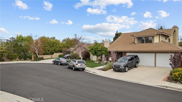 view of front of home with a tile roof, an attached garage, driveway, and a chimney