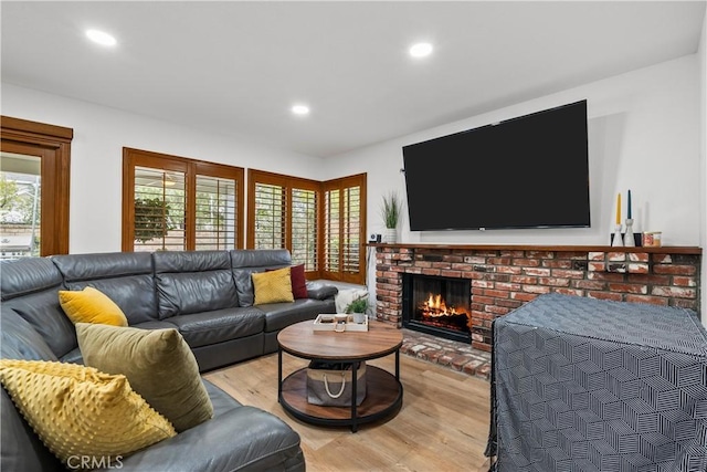 living room with recessed lighting, a brick fireplace, and light wood-type flooring