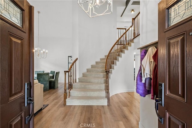 foyer entrance featuring stairs, light wood-style flooring, a high ceiling, and an inviting chandelier