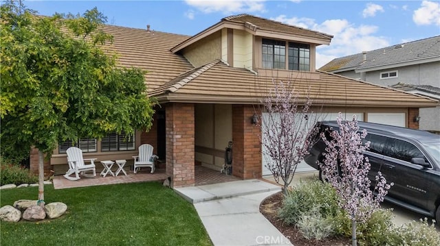 view of front of home with a front yard, a tile roof, brick siding, and a patio area