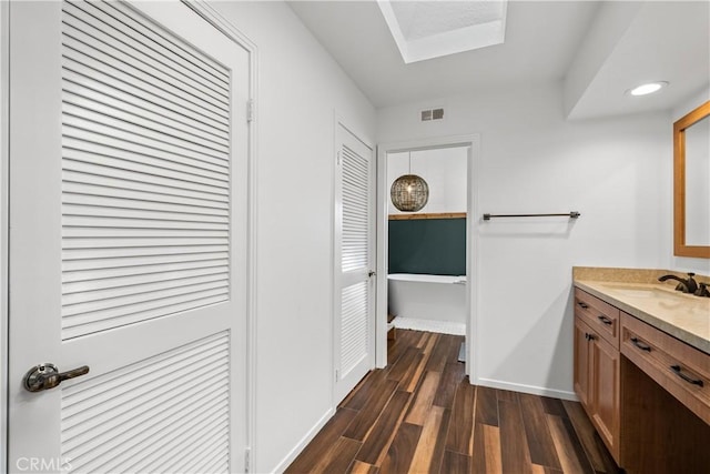 bathroom with a freestanding tub, vanity, baseboards, visible vents, and wood finished floors