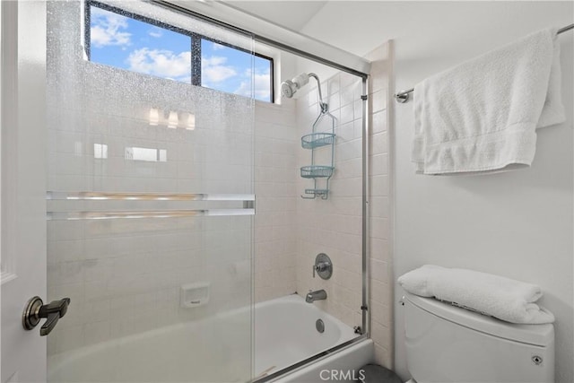 bathroom featuring toilet and shower / bath combination with glass door