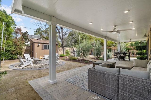 view of patio with an outdoor living space with a fire pit, an outbuilding, ceiling fan, a fenced backyard, and outdoor dining area