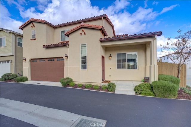 mediterranean / spanish home featuring stucco siding, fence, an attached garage, and a tile roof