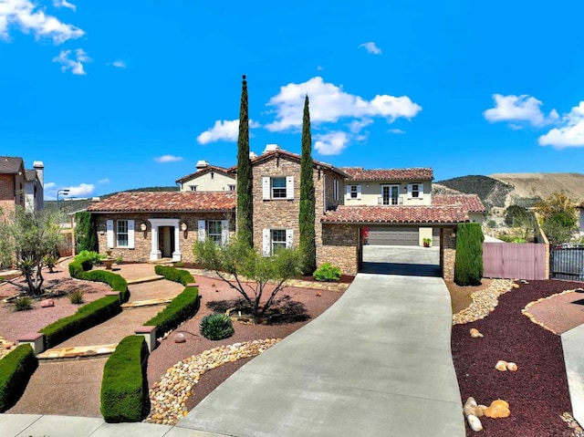 mediterranean / spanish house featuring driveway, stone siding, a tiled roof, an attached garage, and fence