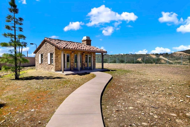 exterior space with fence, a tile roof, a chimney, and stone siding
