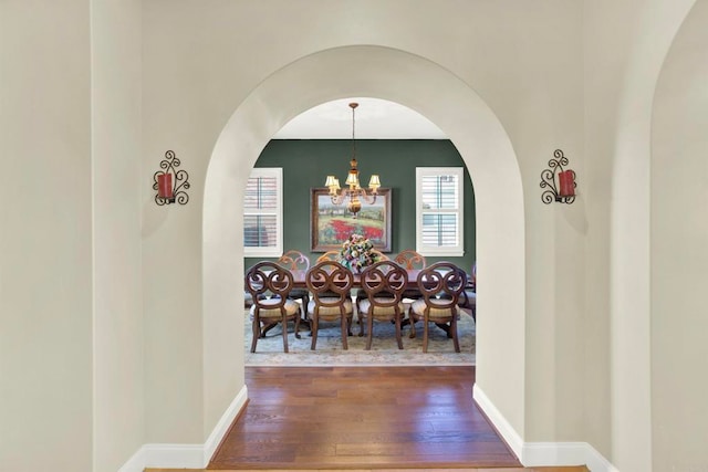 dining room featuring baseboards, arched walkways, a notable chandelier, and wood-type flooring