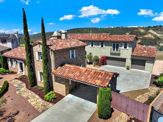 mediterranean / spanish-style house featuring stucco siding, a tile roof, driveway, fence private yard, and stone siding