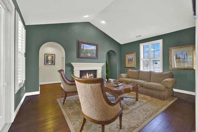 living area featuring arched walkways, a glass covered fireplace, vaulted ceiling, and hardwood / wood-style floors