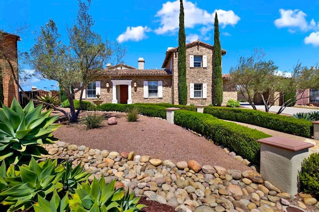 mediterranean / spanish house featuring a chimney, stone siding, and a tiled roof
