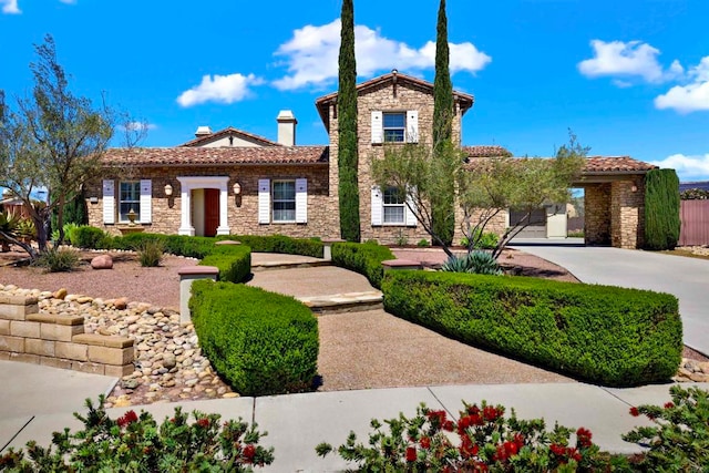 mediterranean / spanish home featuring stone siding, a tile roof, and a chimney