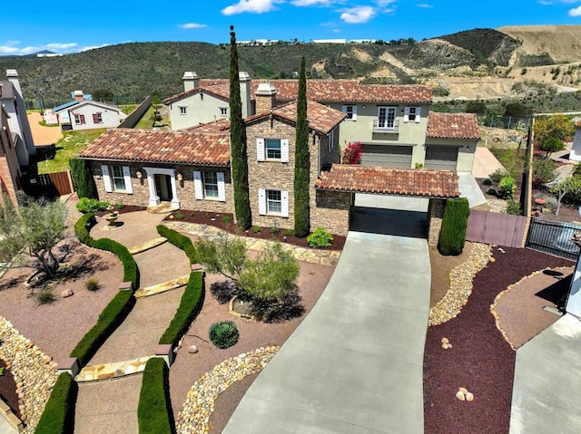mediterranean / spanish-style home featuring a tile roof, driveway, stone siding, fence, and a mountain view