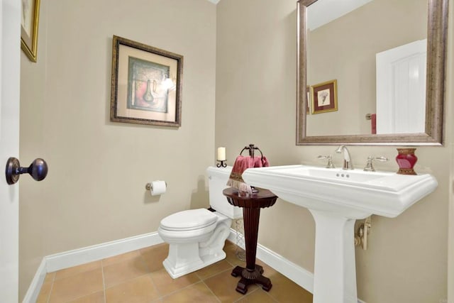 half bath with baseboards, tile patterned flooring, a sink, and toilet