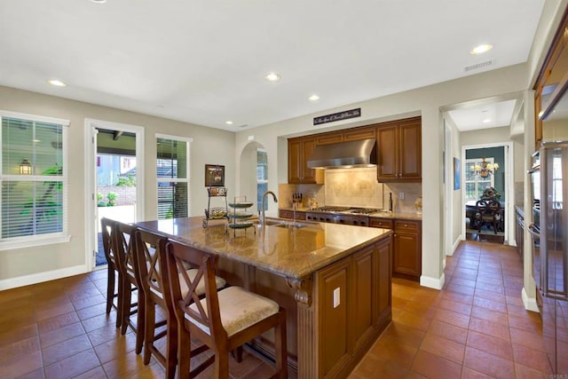 kitchen with arched walkways, baseboards, a sink, and wall chimney range hood