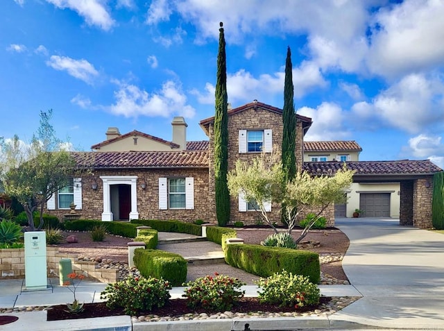 mediterranean / spanish house featuring stone siding, a tile roof, a garage, and concrete driveway