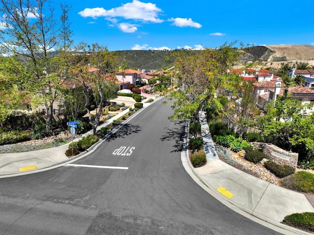 view of road featuring a residential view, curbs, sidewalks, and a mountain view
