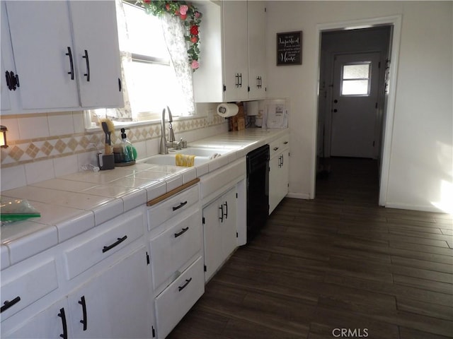 kitchen with a sink, black dishwasher, white cabinetry, decorative backsplash, and dark wood-type flooring
