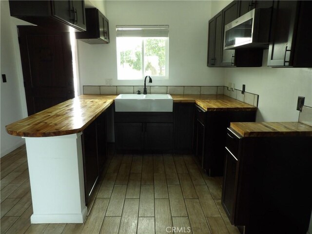 kitchen featuring light wood-type flooring, a sink, a peninsula, and wooden counters