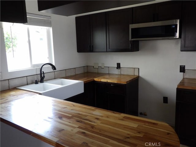 kitchen featuring dark cabinets, a sink, wood counters, and stainless steel microwave