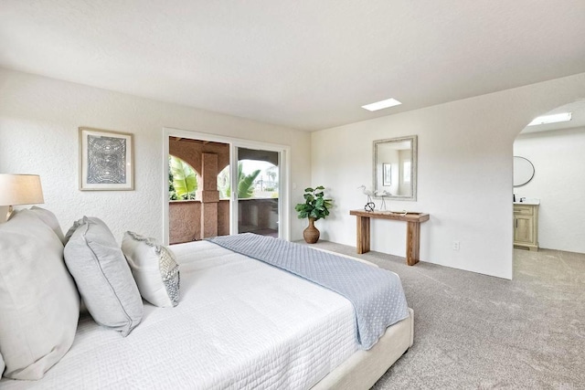 bedroom with access to outside, carpet flooring, ensuite bath, and arched walkways