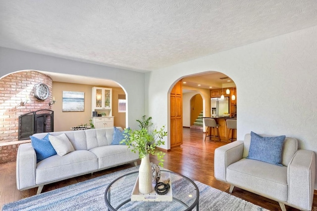 living room with arched walkways, a textured ceiling, a brick fireplace, and hardwood / wood-style flooring