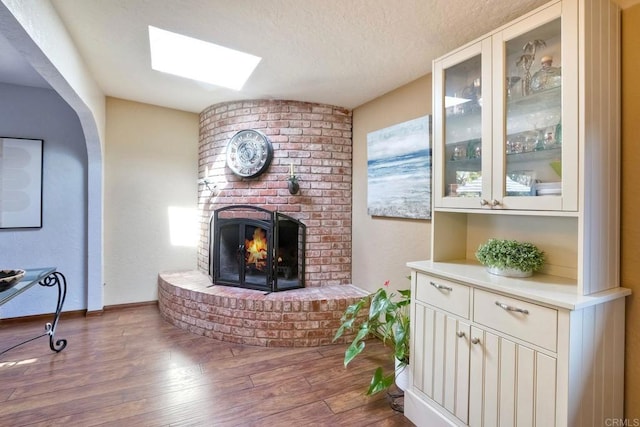 living area with arched walkways, a textured ceiling, a fireplace, wood finished floors, and a skylight