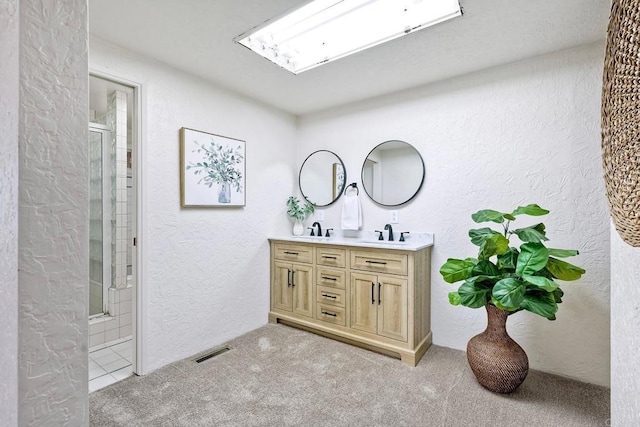 bathroom with a textured wall, visible vents, an enclosed shower, and a sink