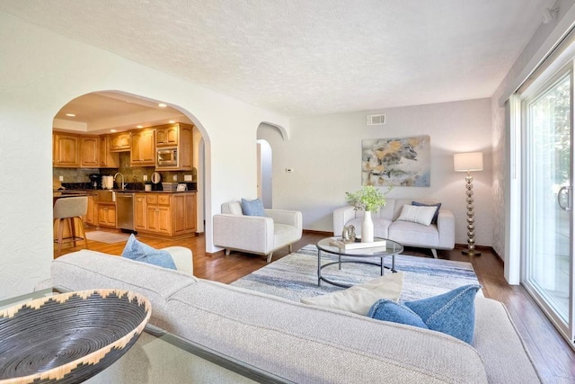 living room with baseboards, a textured ceiling, light wood-style floors, visible vents, and arched walkways
