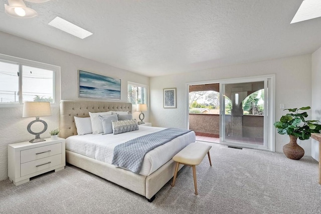 bedroom featuring access to outside, a textured ceiling, visible vents, a skylight, and light colored carpet