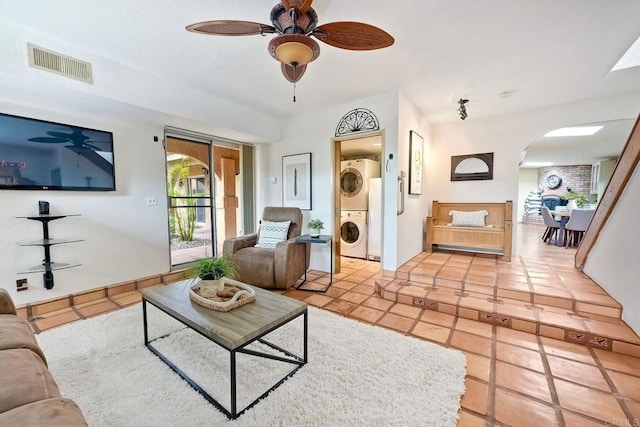 living area featuring a ceiling fan, light tile patterned flooring, stacked washer / dryer, visible vents, and arched walkways