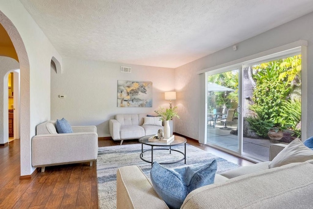 living area featuring visible vents, baseboards, arched walkways, a textured ceiling, and hardwood / wood-style floors