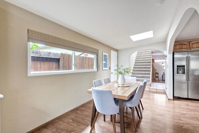 dining area featuring baseboards, arched walkways, light wood-style floors, and stairs