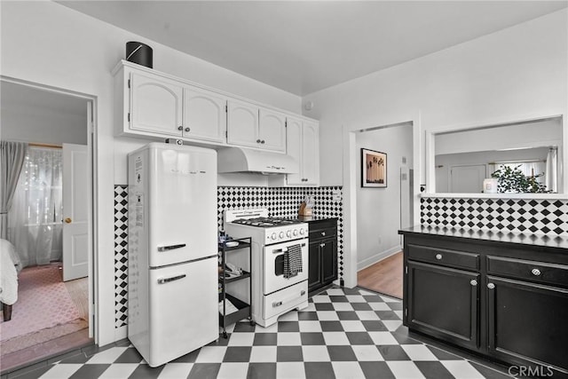 kitchen featuring white range with gas stovetop, white cabinets, dark floors, and freestanding refrigerator