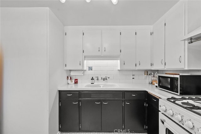 kitchen with backsplash, a sink, stainless steel microwave, white cabinets, and dark cabinets