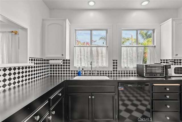 kitchen featuring a sink, dishwasher, white cabinets, decorative backsplash, and white microwave