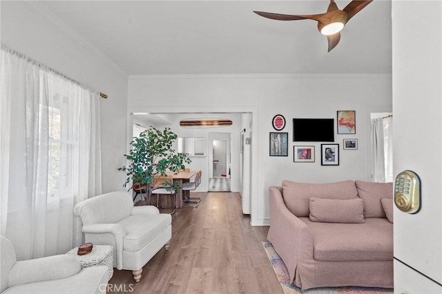 living area with ornamental molding, light wood-style floors, and a ceiling fan