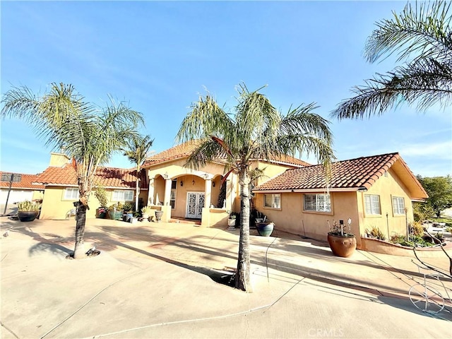 mediterranean / spanish house with a tile roof, stucco siding, and french doors