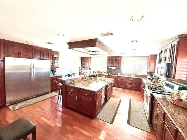 kitchen featuring visible vents, stainless steel fridge, light wood finished floors, gas stove, and glass insert cabinets