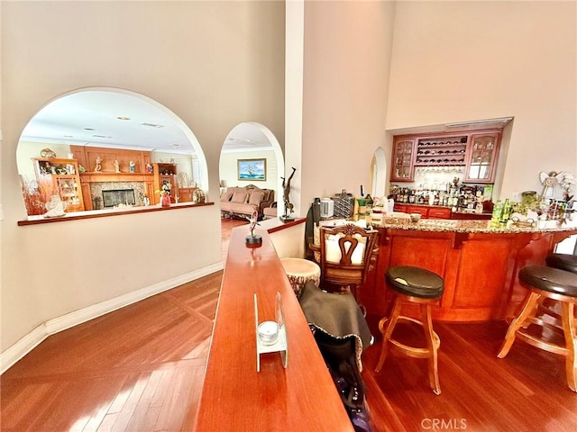bar featuring a towering ceiling, a dry bar, baseboards, and wood finished floors