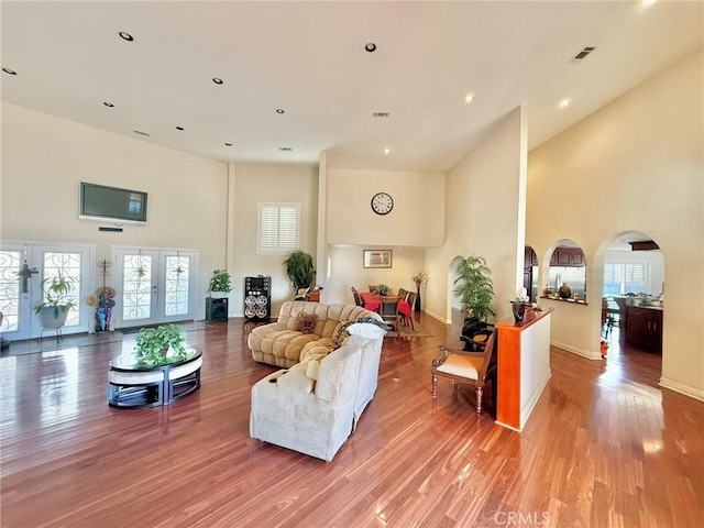 living area with a towering ceiling, arched walkways, visible vents, and light wood-type flooring