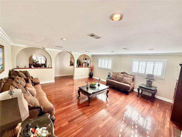 living room with baseboards, visible vents, wood finished floors, and crown molding