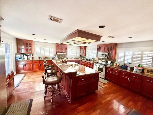 kitchen featuring visible vents, range with gas stovetop, a breakfast bar, stainless steel microwave, and dark brown cabinets