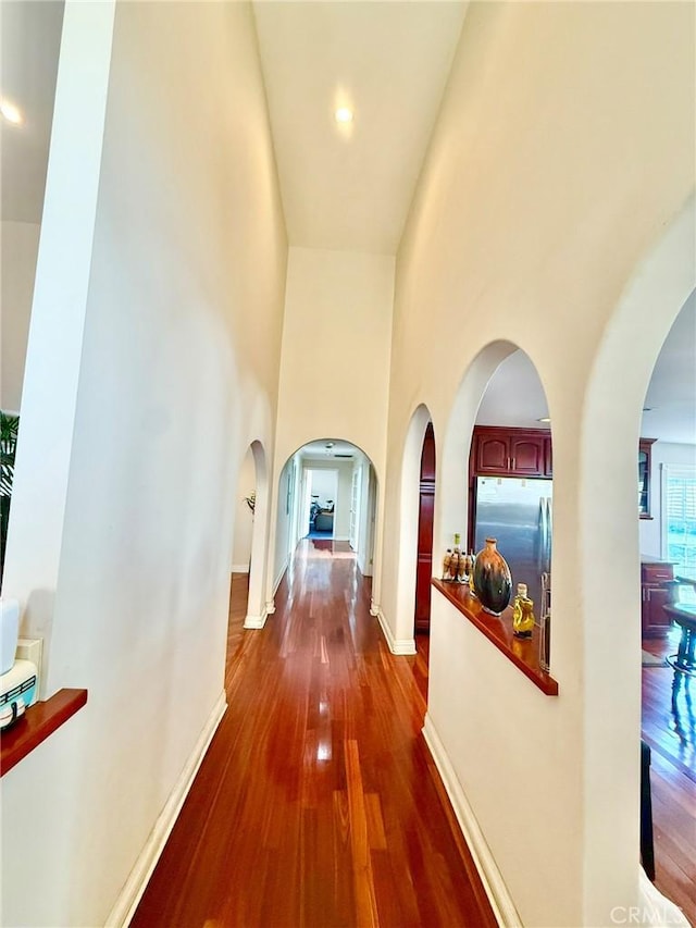 hallway featuring dark wood finished floors, baseboards, a high ceiling, and arched walkways
