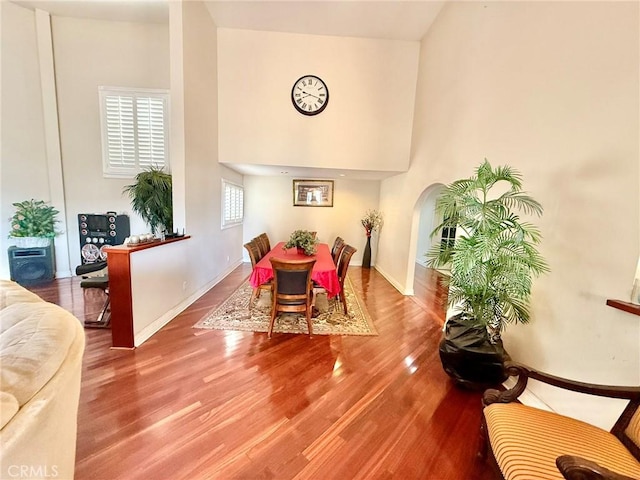 dining space featuring baseboards, arched walkways, a high ceiling, and wood finished floors
