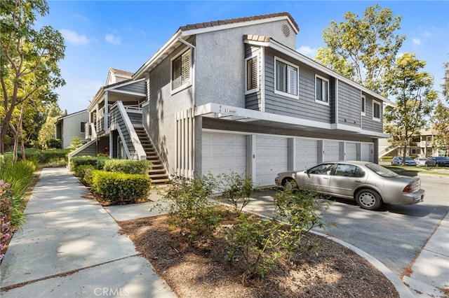 view of property exterior featuring driveway, stairway, stucco siding, and a garage