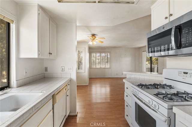 kitchen featuring white appliances, tile countertops, light wood-type flooring, and a healthy amount of sunlight